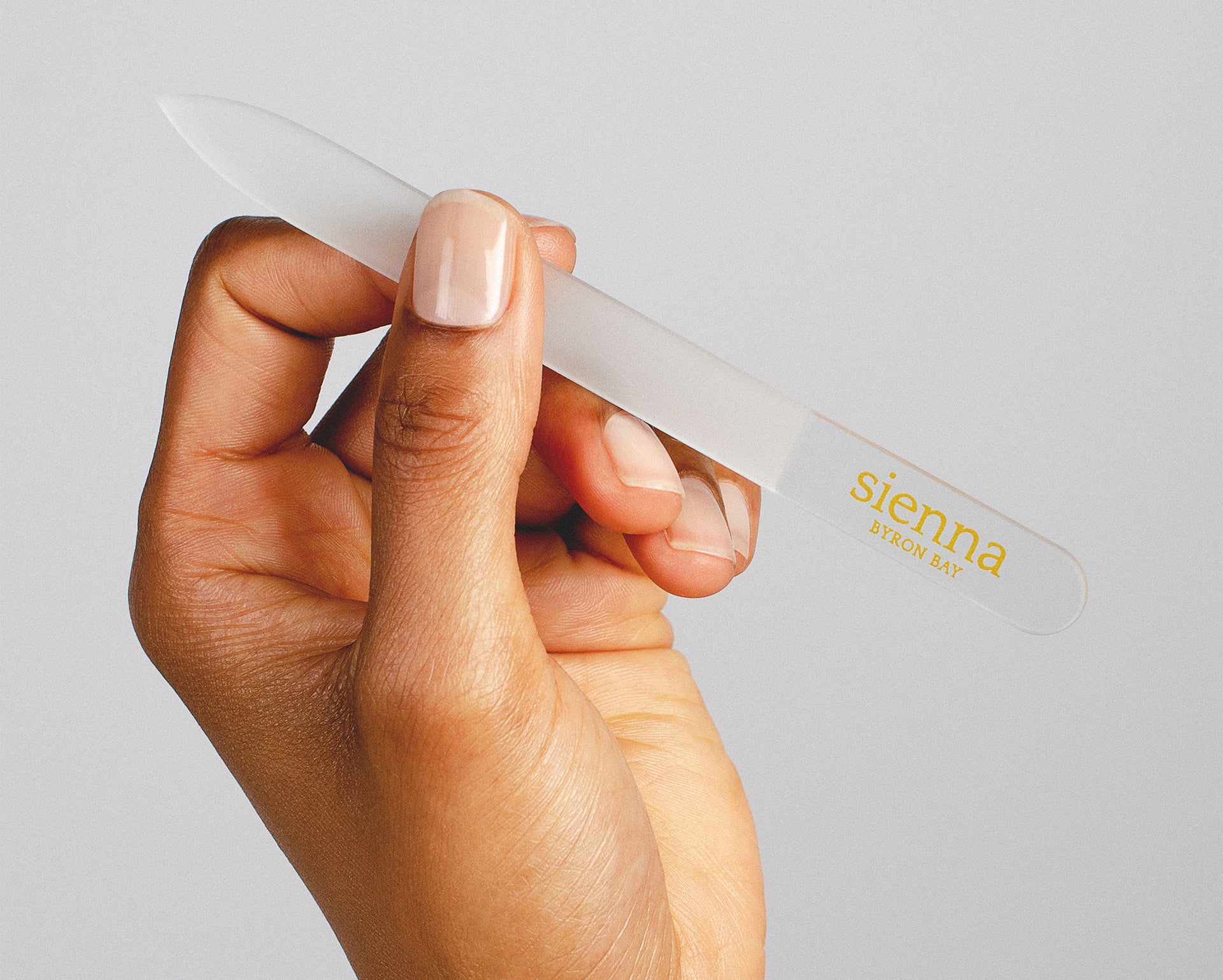 Hand holding a clear glass nail file, demonstrating proper tool for filing nails