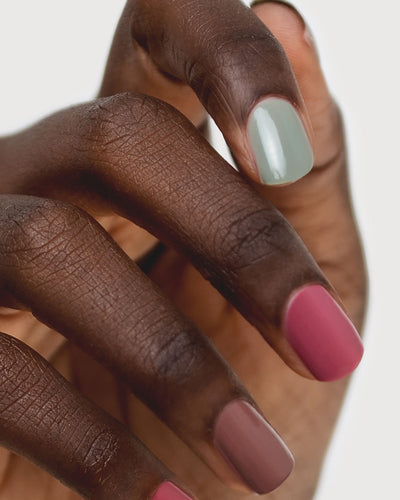 Dark skin hand wearing Soundscape sage green crème, Heartspace raspberry sorbet crème and Grounded mylk chocolate crème nail polish by Sienna.