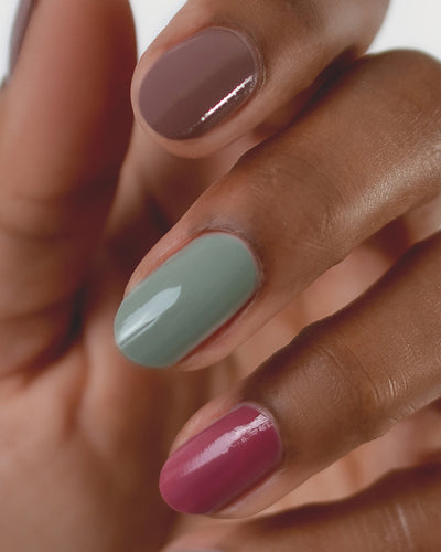 Medium skin hand wearing Soundscape sage green crème, Heartspace raspberry sorbet crème and Grounded mylk chocolate crème nail polish by Sienna.