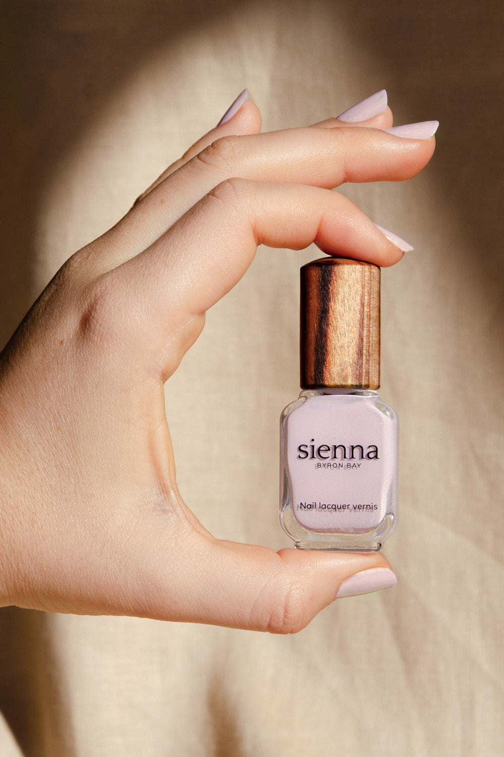 Tranquility Light Mauve Rose Crème nail polish by Sienna Byron Bay on fair skin tone hands holding bottle with timber lid.