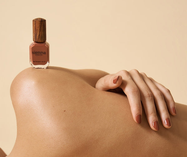 red nail polish on fair skin models shoulder on beige background by sienna