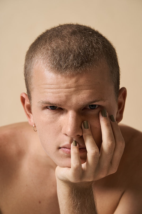 young man wearing green nail polish by sienna and resting his head on his hand