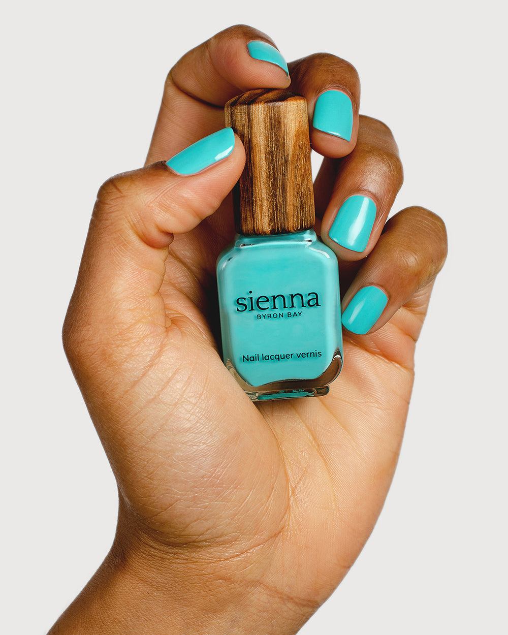 Turquoise aqua nail polish hand swatch on medium skin tone holding a sienna bottle