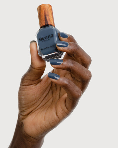Dark granite blue-grey nail polish hand swatch on dark skin tone holding sienna bottle