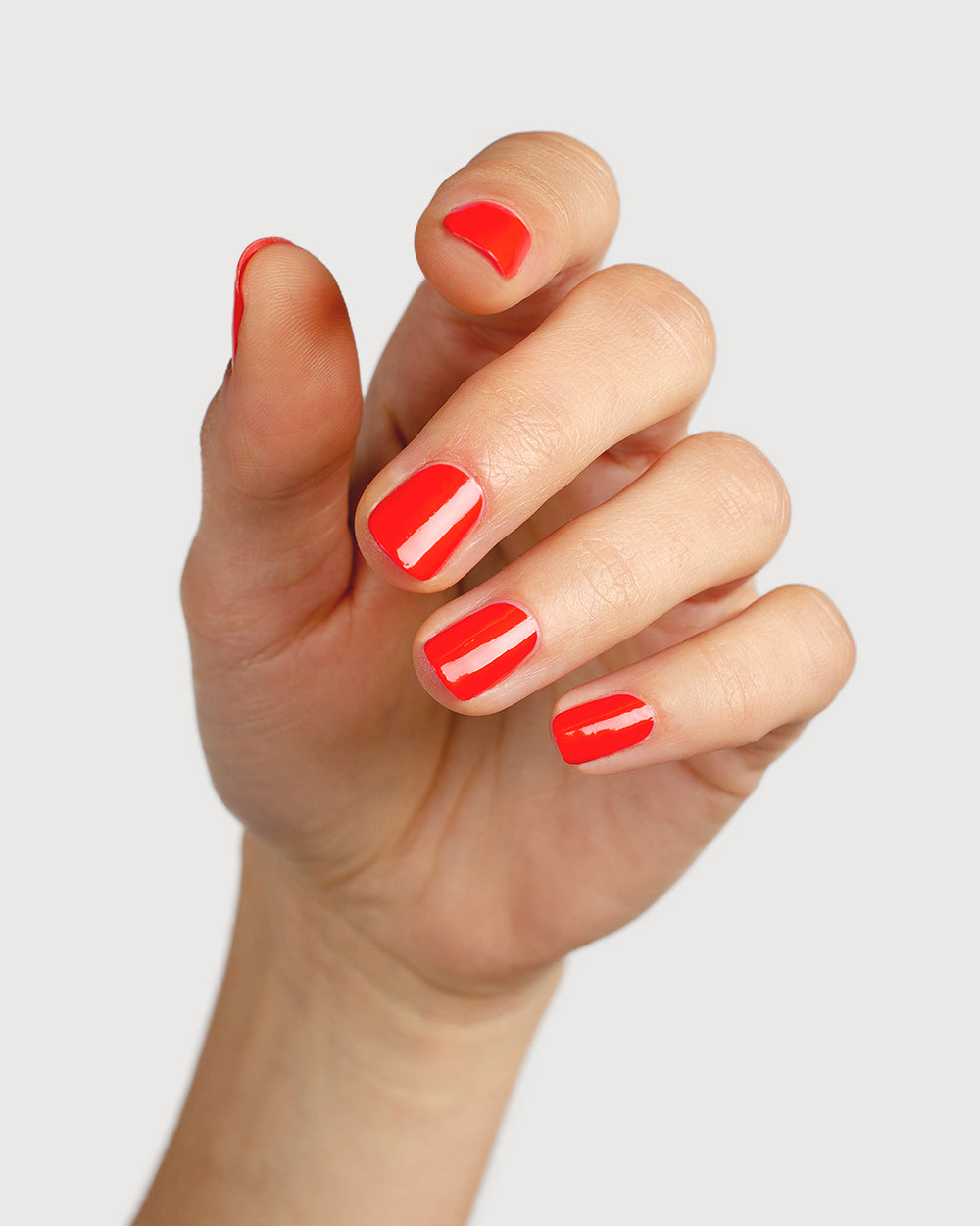 Warm strawberry red nail polish hand swatch on fair skin tone
