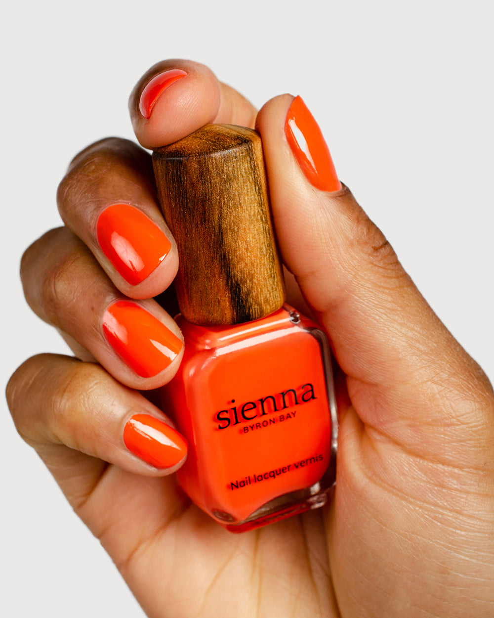 Tangerine nail polish hand swatch on medium skin tone holding sienna bottle