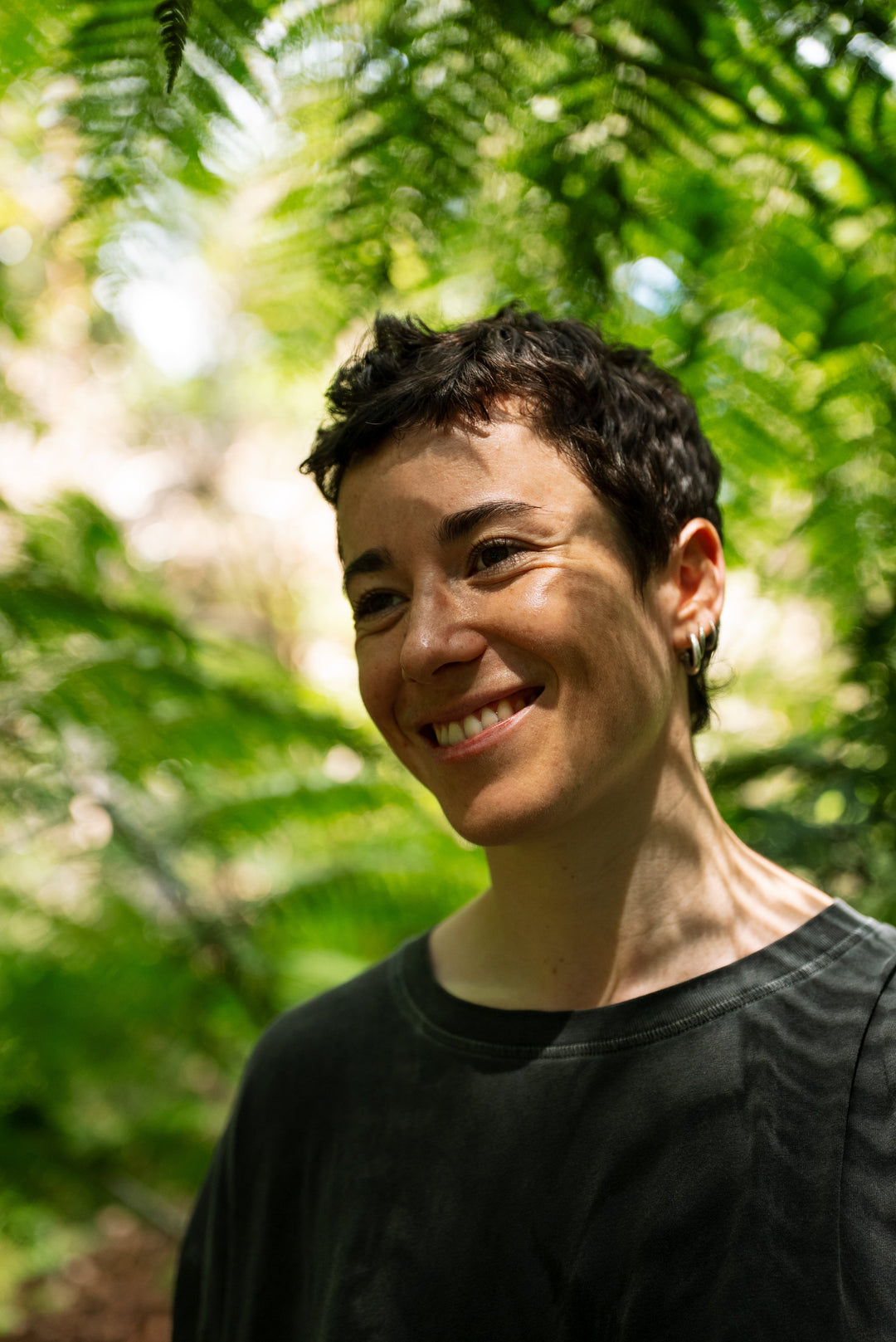 A smiling woman with short dark hair standing in front of lush green ferns.