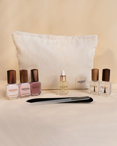 trio of white and pink nail polish with timber caps sitting to the left and a duo of clear nail polish sitting to the right with a glass nail file and cuticle oil bottle sitting in front of a white corduroy bag