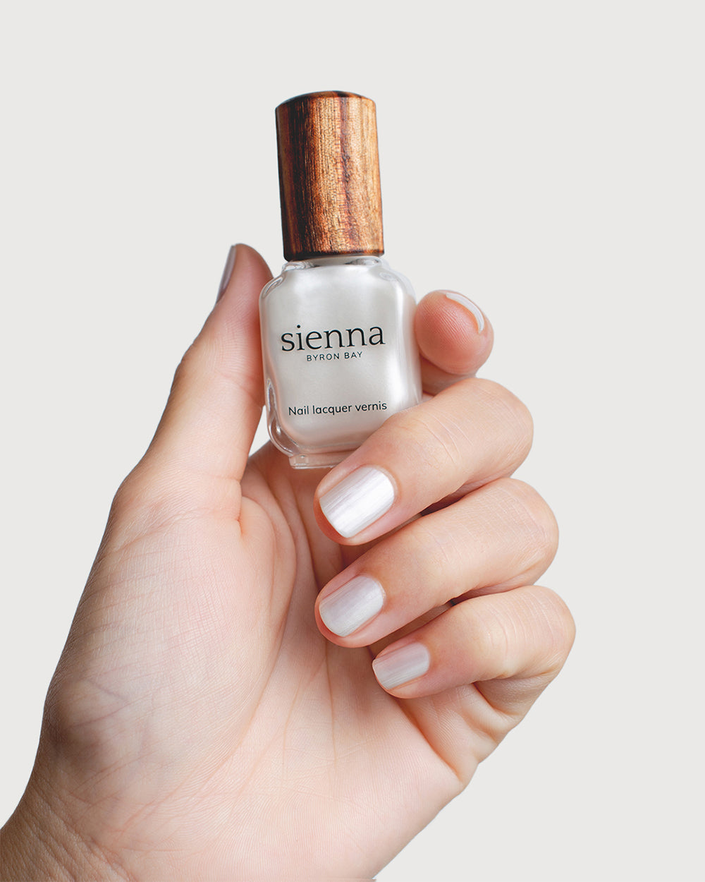 Aura nail polish hand swatch on fair skin tone holding sienna bottle