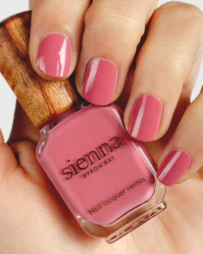 midtone pink nail polish hand swatch on fair skin tone, holding a Sienna Bottle