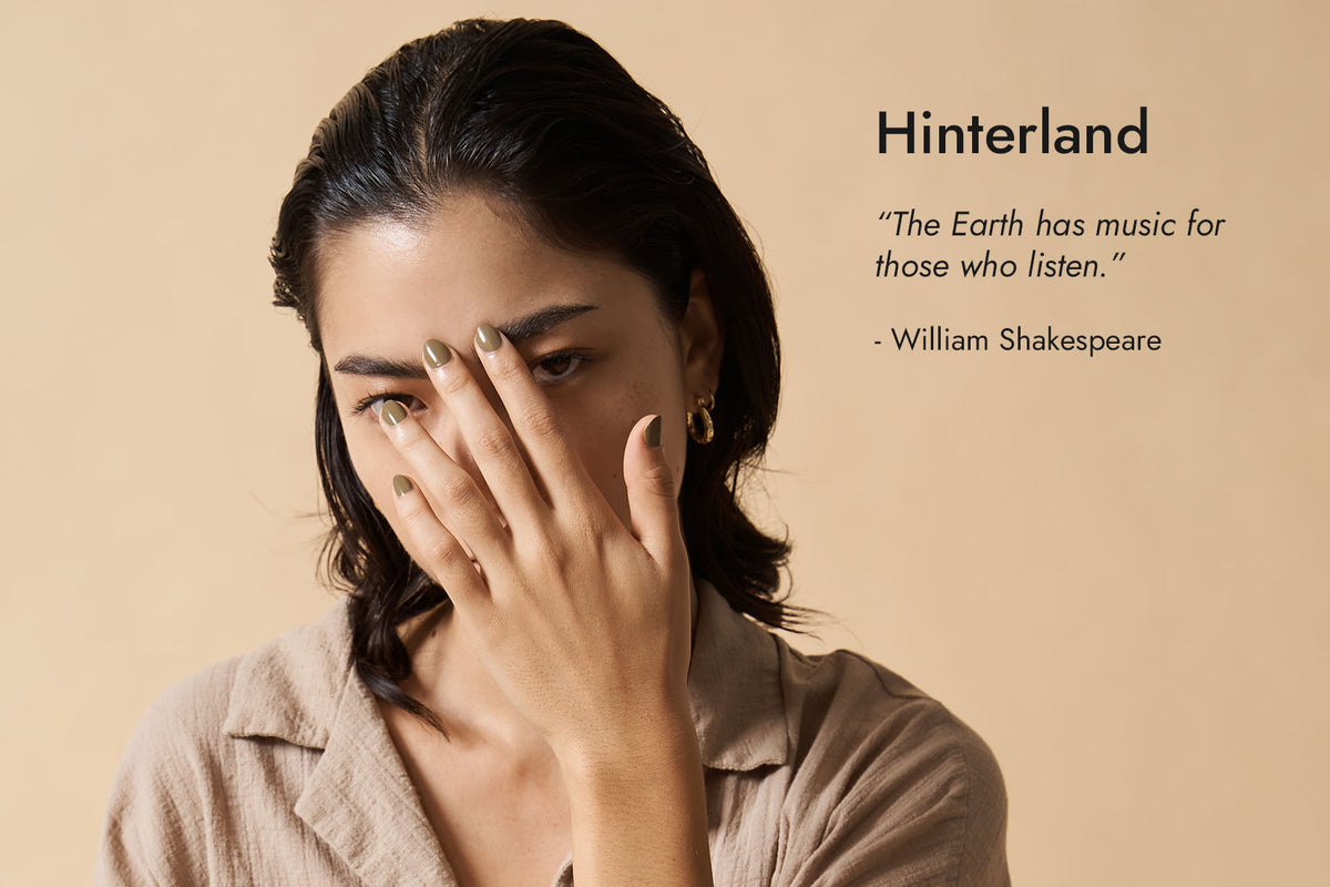 Woman with tan skin tone wearing Wilderness khaki green nail polish with hand on face, Hinterland text and quote.