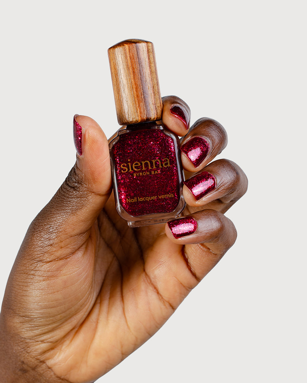 Dark skin tone hand with Starlit Rose metallic shimmer glaze nail colour holding Sienna Starlit Rose bottle with signature timber cap