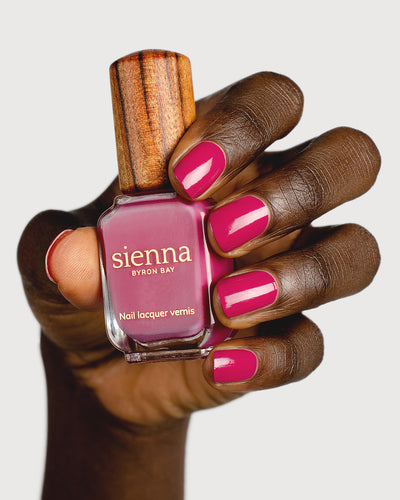 fuschia pink nail polish hand swatch on dark skin tone holding a Sienna Bottle 