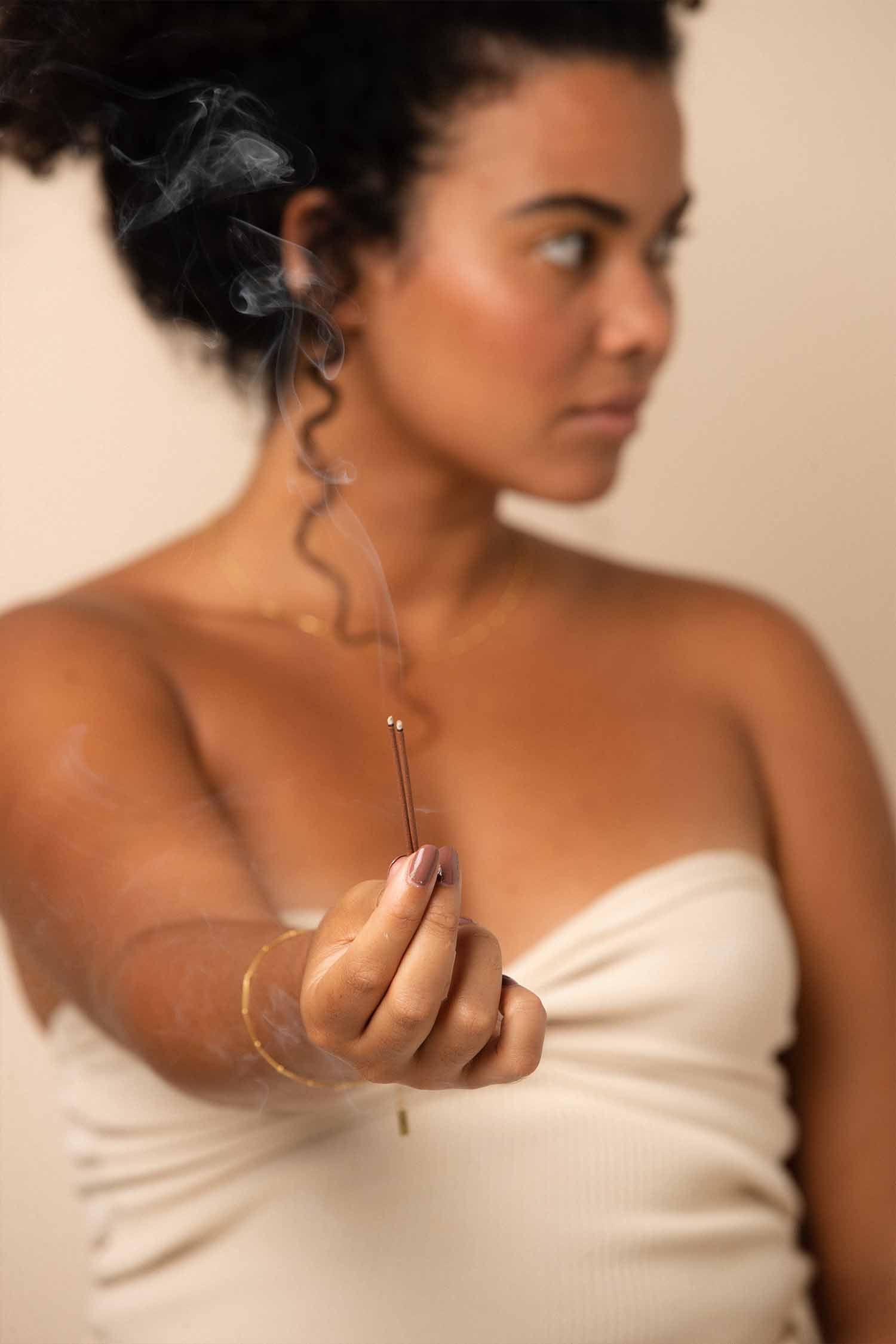 Woman with dark skin and freckles wearing Grounded chocolate mylk nail polish by Sienna Byron Bay and holding incense