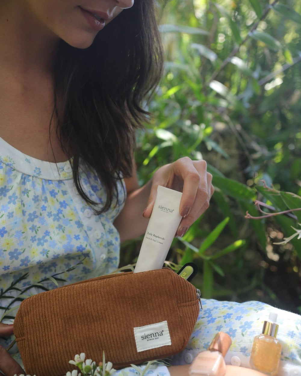 Woman holding a brown pouch with a skincare product, surrounded by greenery