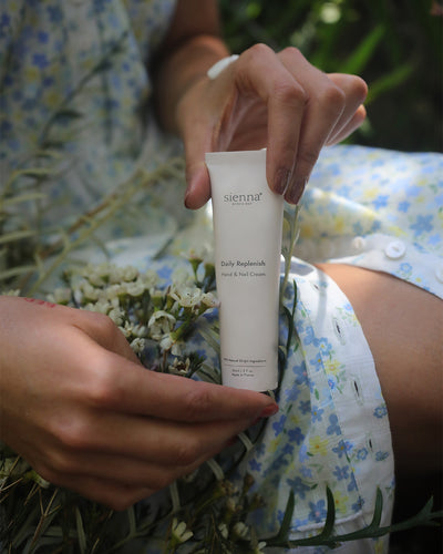 Person holding a hand and nail cream tube labeled 'sienna' with a natural background
