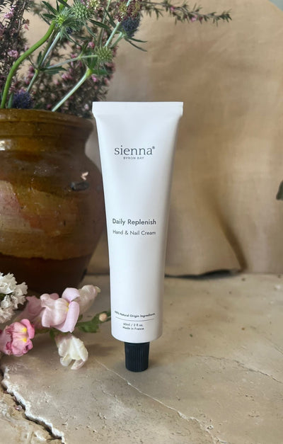 Tube of sienna daily replenish hand & nail cream on a stone surface with flowers and a vase in the background