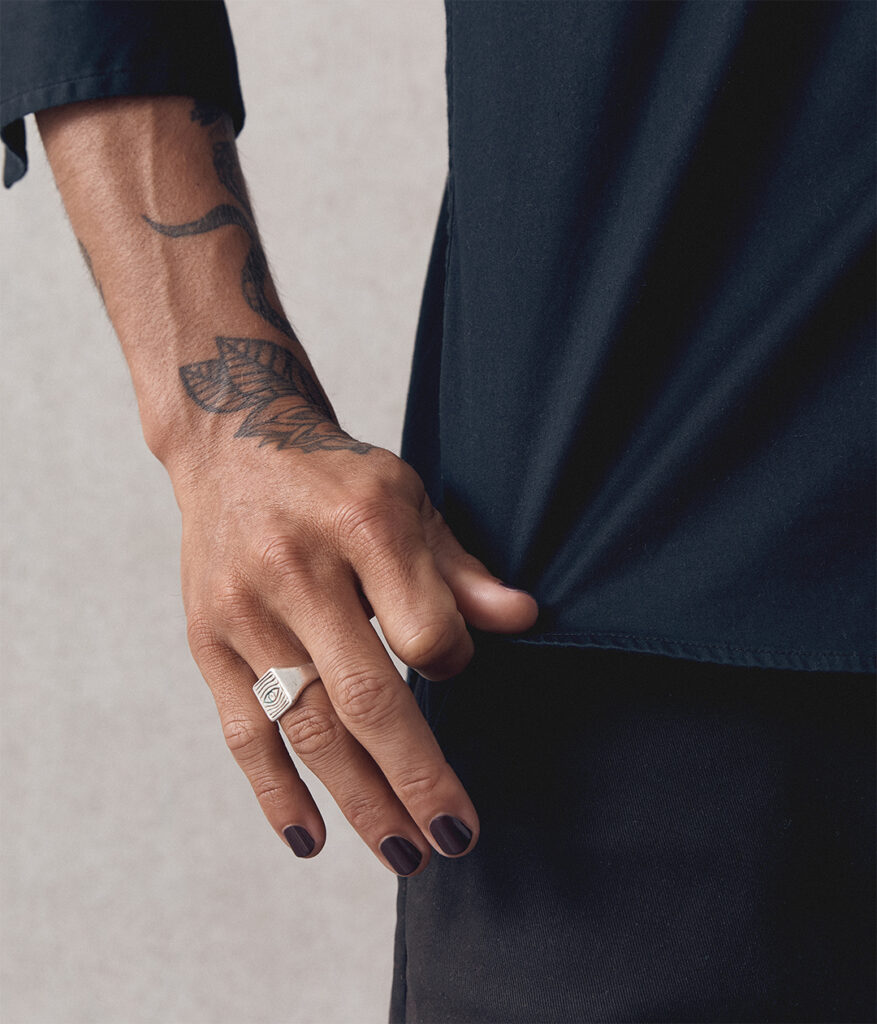 close up of man's hand holding his black shirt down and wearing dark aubergine nail polish by sienna