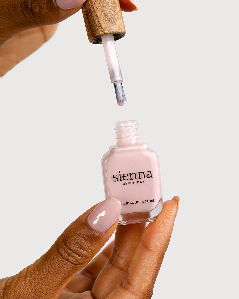 Medium skin tone hand with Amour soft pink crème nail colour and long, strong and healthy natural nails holding an open bottle of Sienna Nail Colour crème showing our patented wide brush for easy application every time.