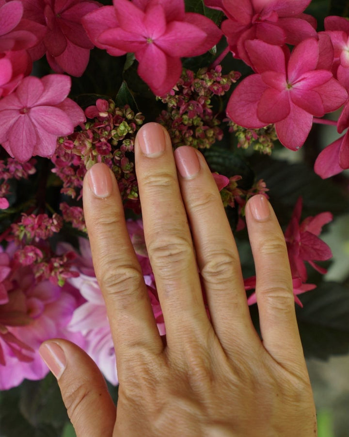 Medium skin tone hands with painted natural nails in Stone Sienna nail polish creme glaze against pink flowers