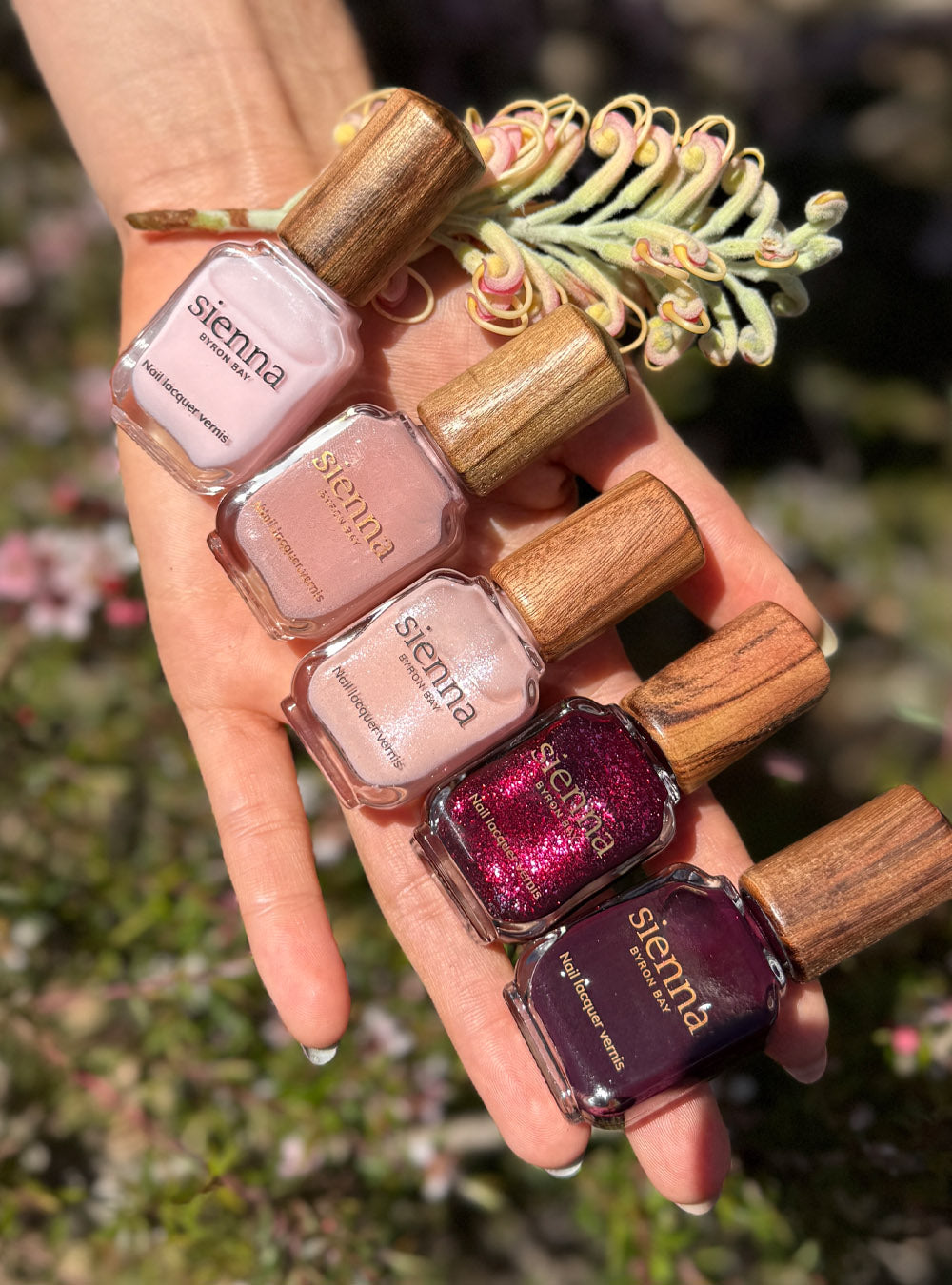 A fair skin hand outstretched showcasing the Midsummer  collection bottles in soft pink and reds with signature timber caps