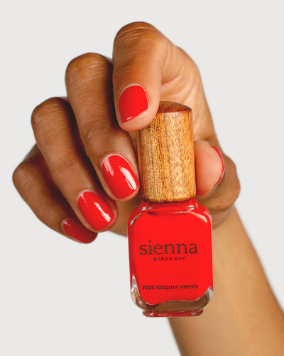 bright red nail polish hand swatch on Medium skin tone holding sienna bottle