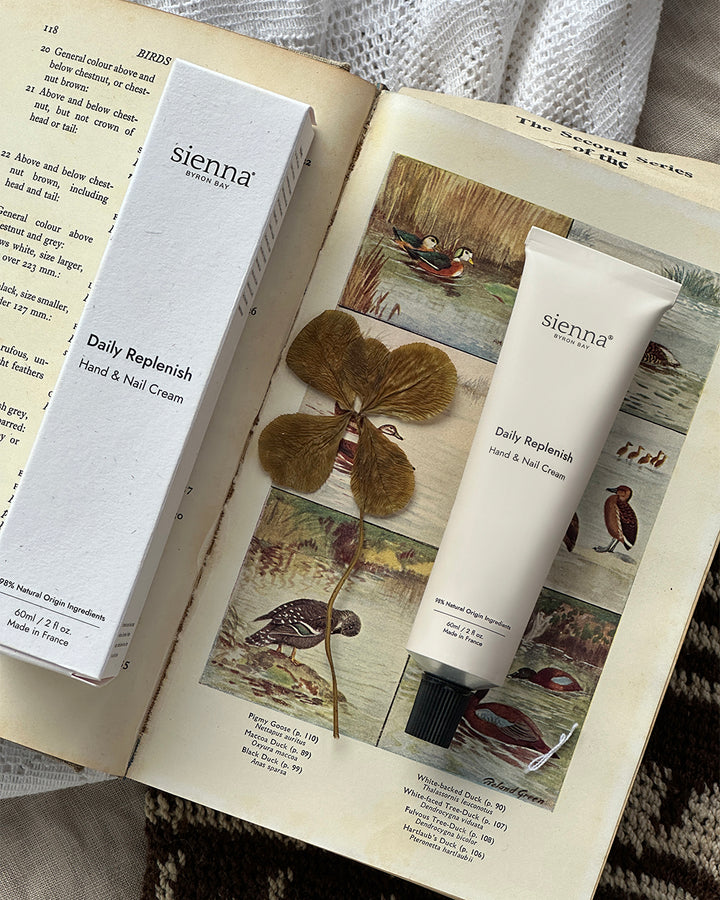Sienna Daily Replenish Hand &amp; Nail Cream on an open book with a natural background