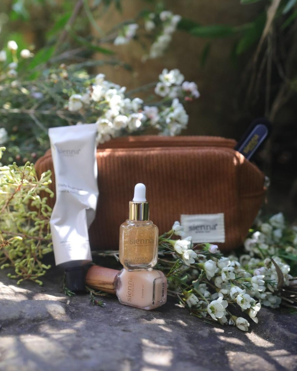 Cosmetic bag with skincare products and flowers on a stone surface