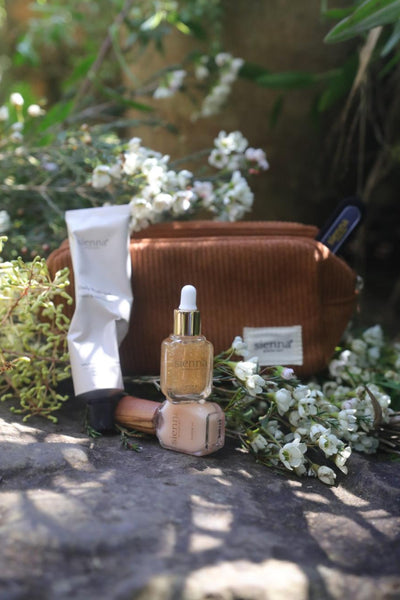 Cosmetic bag with skincare products on a stone surface with flowers in the background