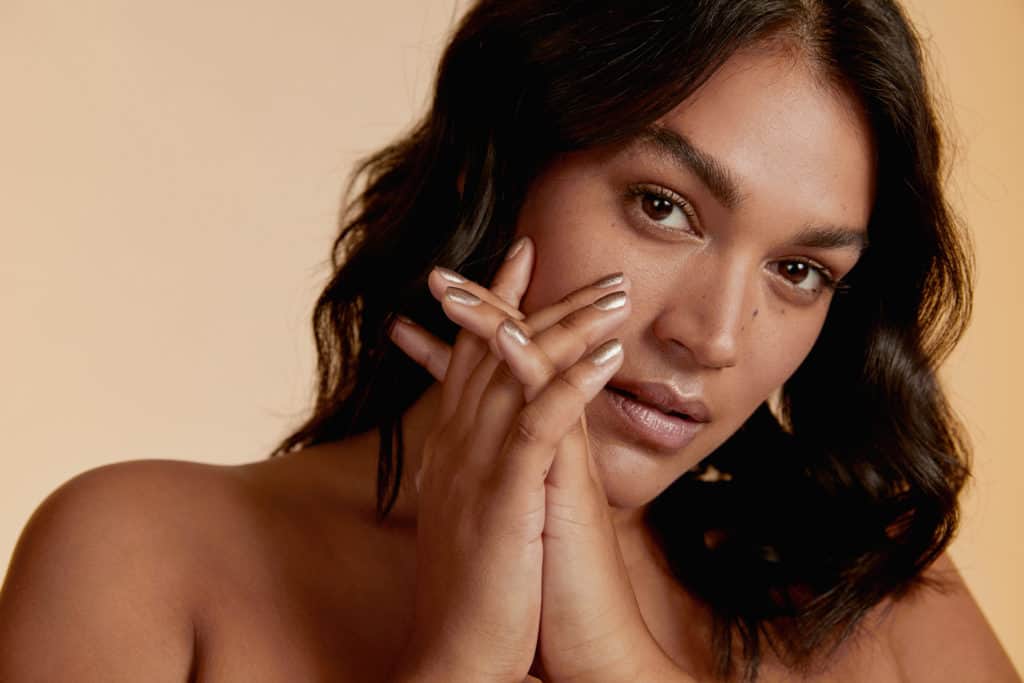 medium skin tone model wearing nude crushed crystal nail polish by sienna on beige background