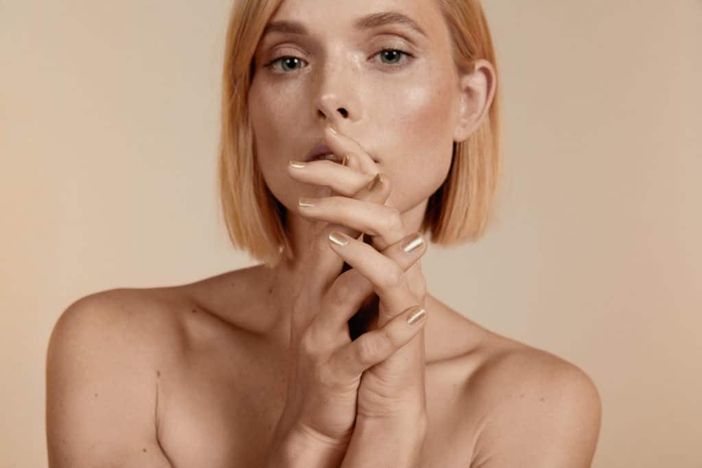 naked fair skin model wearing gold crushed crystal nail polish by sienna on beige background