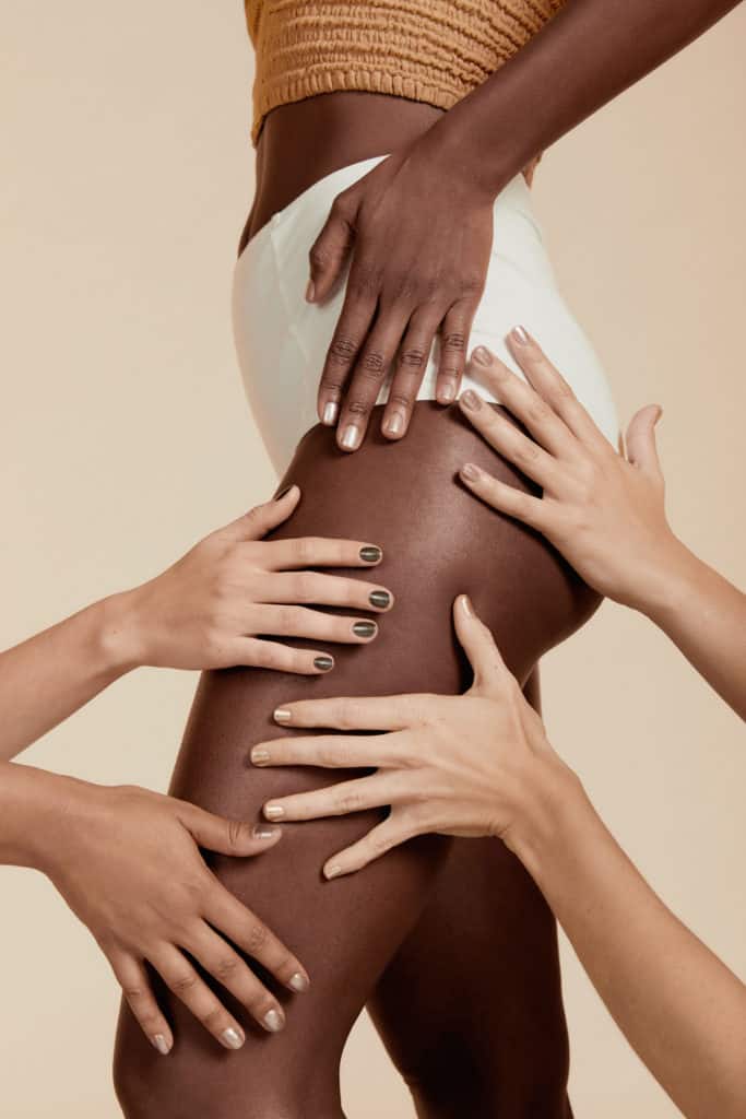 different skin tone models placing their hands on a dark skin model's thigh wearing crushed crystal nail polish by sienna