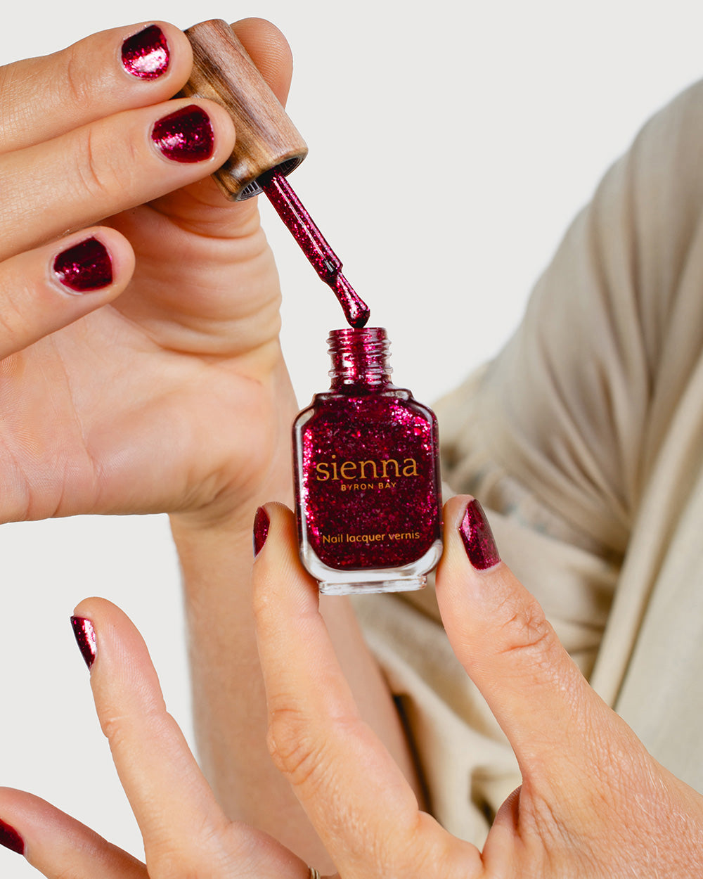 Fair skin tone hand holding a Sienna Byron Bay nail lacquer vernis bottle with signature timber cap in sparkly colour Starlit Rose. Nails are strong, and healthy and painted in sparkly Starlit Rose glaze.