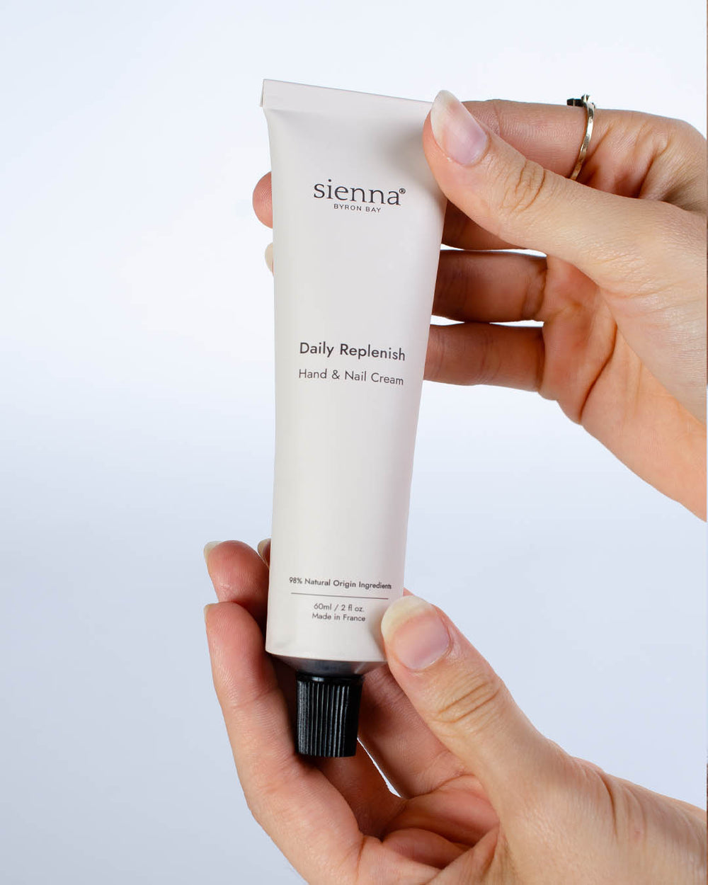 Hand holding a tube of sienna Daily Replenish Hand & Nail Cream against a light background