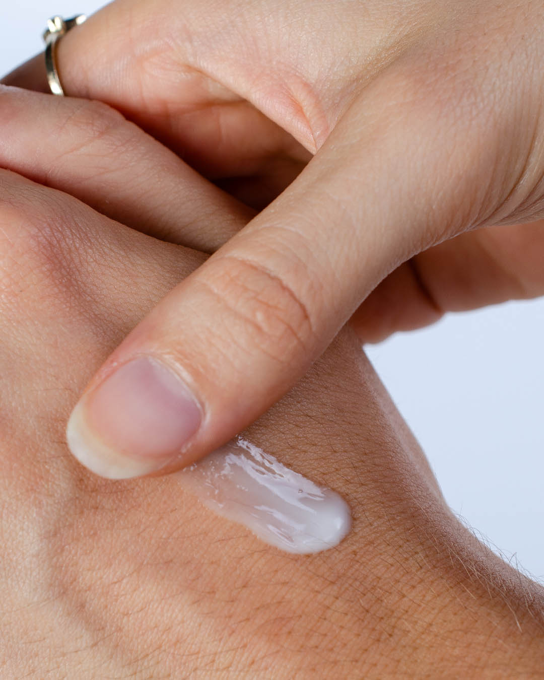 Hand applying a small amount of cream to the wrist with a white background