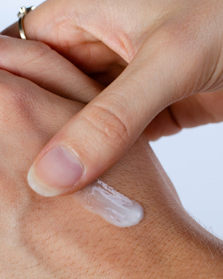 Hand applying a small amount of cream to the wrist with a white background