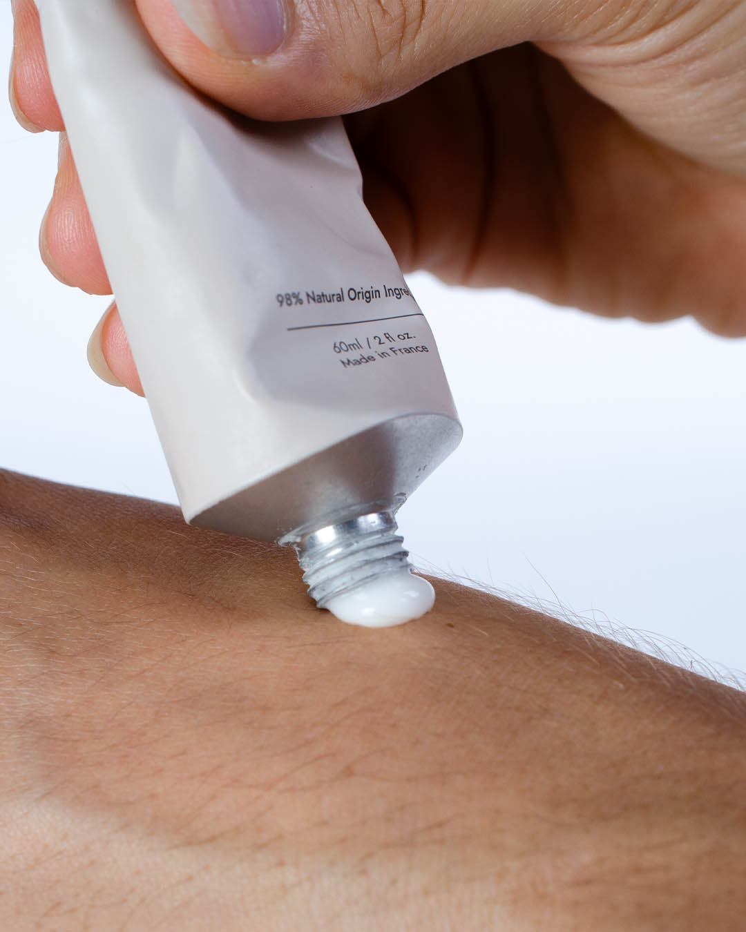 Tube of Sienna Daily Replenish Hand &amp; Nail being squeezed onto fair skin tone hand on plain white background. Label reads- 98% Natural Origin Ingredients