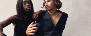 dark skin young woman and fair skin young man with long hair wearing chic black and navy shirts wearing navy blue nail polish by sienna with concrete wall on the background