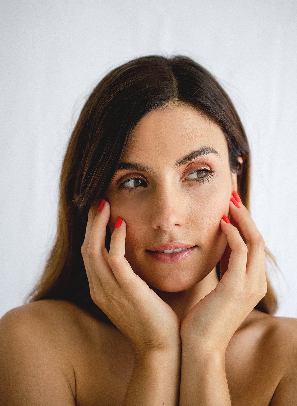 young caucasian woman holding her hands to her face wearing red nail polish by sienna