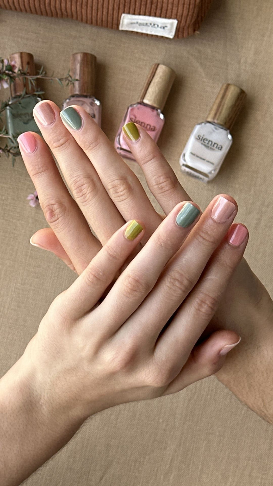 Close-up of hands with painted nails and a row of nail polishes on a wooden surface.