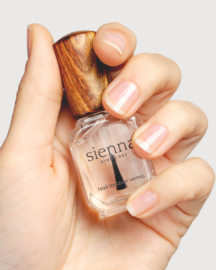 clear base coat nail polish hand swatch on fair skin tone holding a sienna bottle