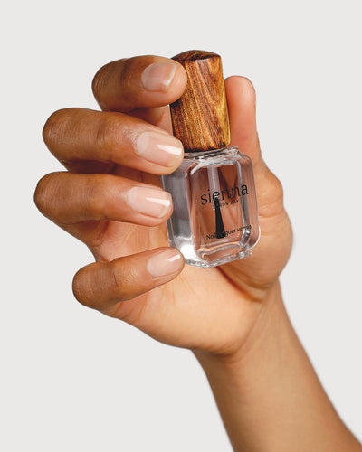 clear base coat nail polish hand swatch on medium skin tone holding a sienna bottle