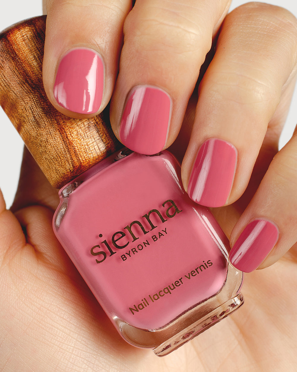 midtone pink nail polish hand swatch on fair skin tone holding a sienna bottle up close