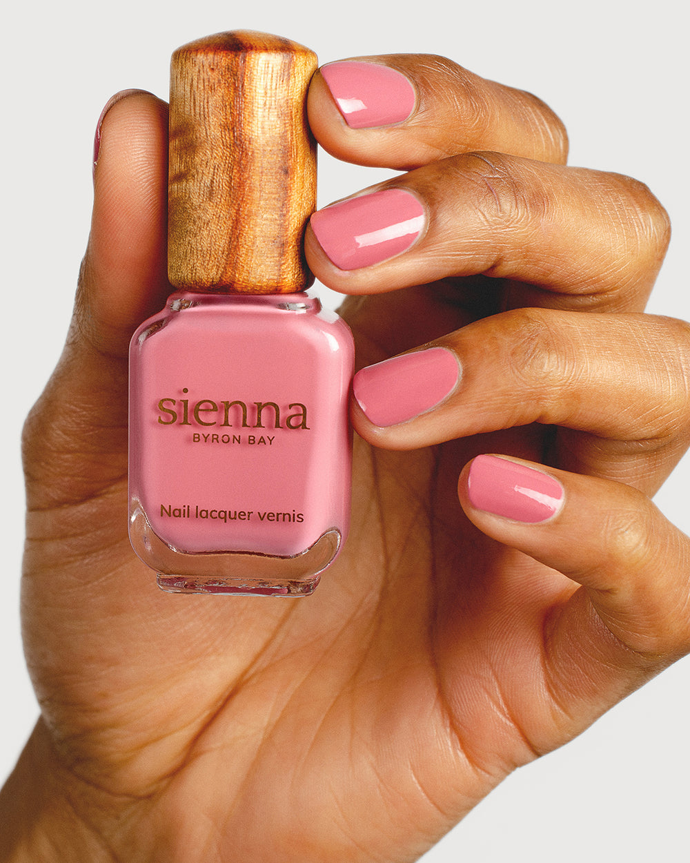 midtone pink nail polish hand swatch on medium skin tone holding a sienna bottle