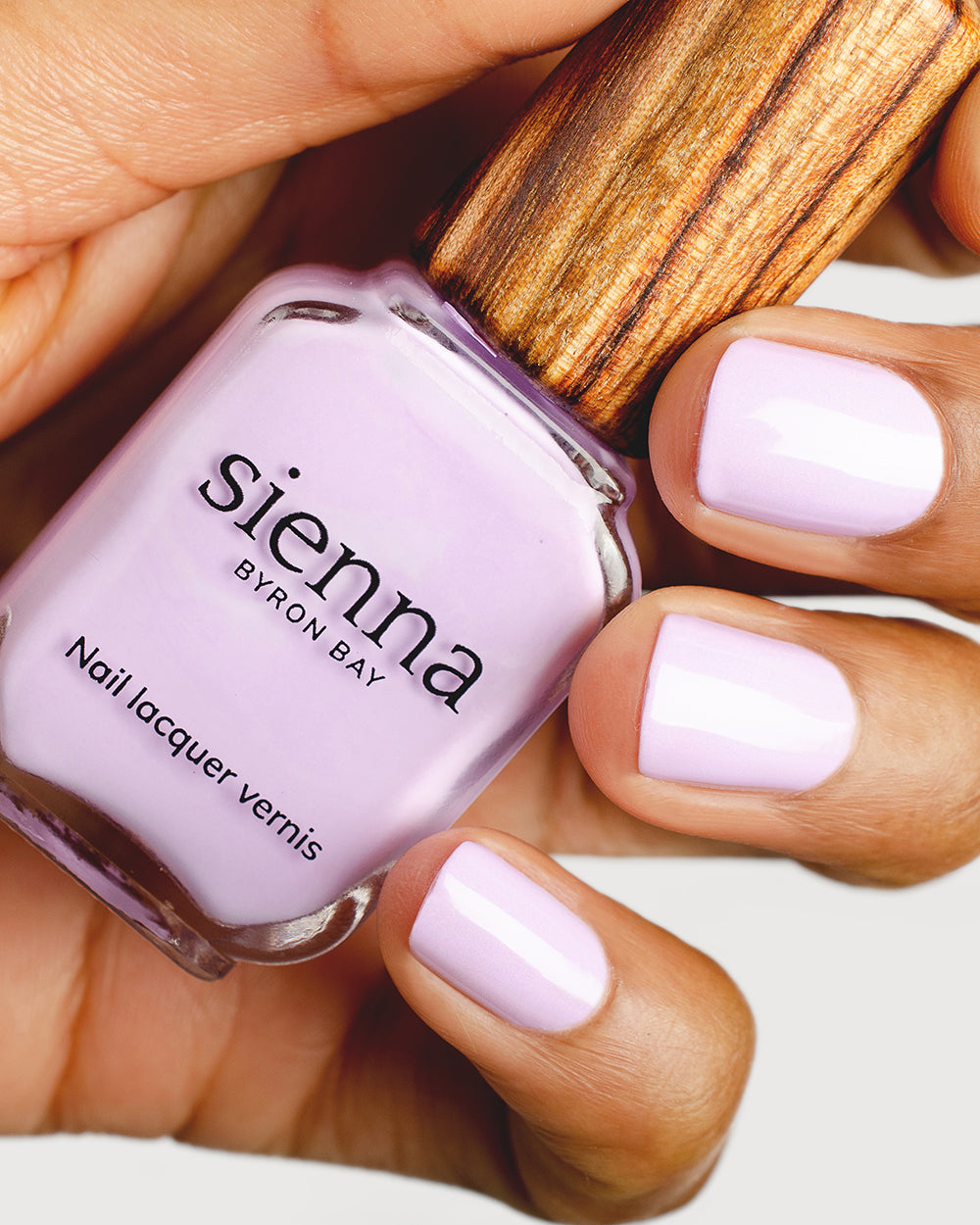 lilac purple nail polish hand swatch on medium skin tone holding a sienna bottle up close