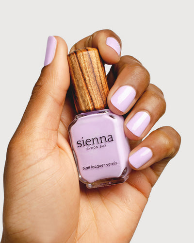 lilac purple nail polish hand swatch on medium skin tone holding a sienna bottle