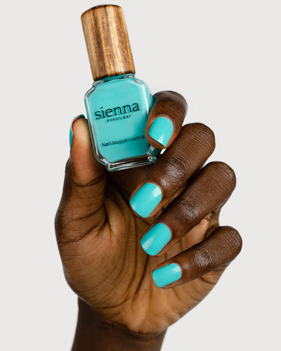 Turquoise aqua nail polish hand swatch on dark skin tone holding a sienna bottle