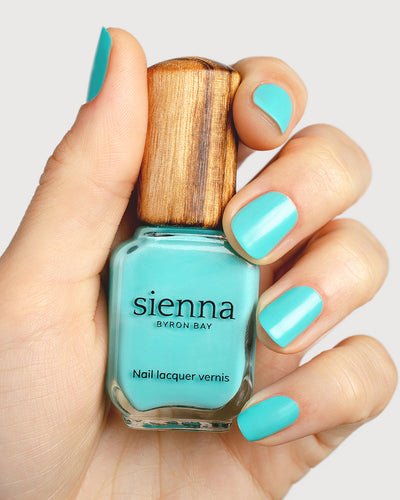 turquoise aqua nail polish hand swatch on fair skin tone holding a sienna bottle up close