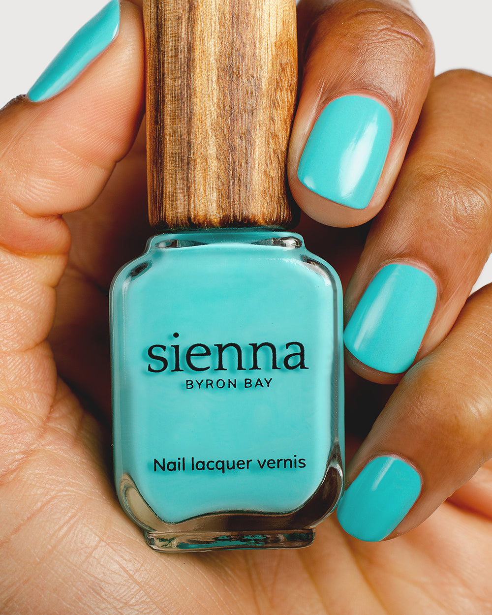 Turquoise aqua nail polish hand swatch on medium skin tone holding a sienna bottle up close