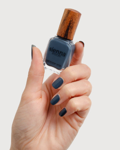 Dark granite blue-grey nail polish hand swatch on fair skin tone holding sienna bottle